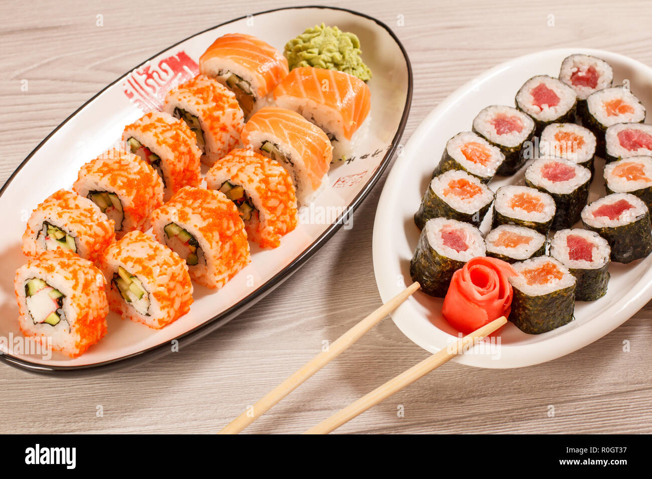 Verschiedene sushi Rollen mit Reis, Gemüse, Fisch und Meeresfrüchte auf keramischen Platten auf hölzernen Schreibtisch. Ansicht von oben Stockfoto