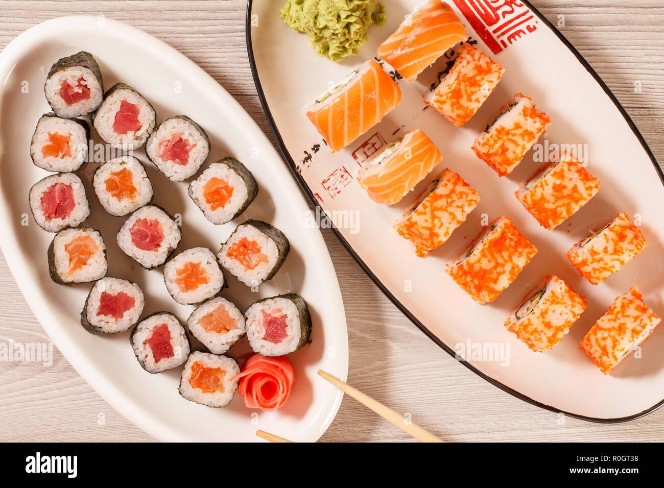 Verschiedene sushi Rollen mit Reis, Gemüse, Fisch und Meeresfrüchte auf keramischen Platten auf hölzernen Schreibtisch. Ansicht von oben Stockfoto