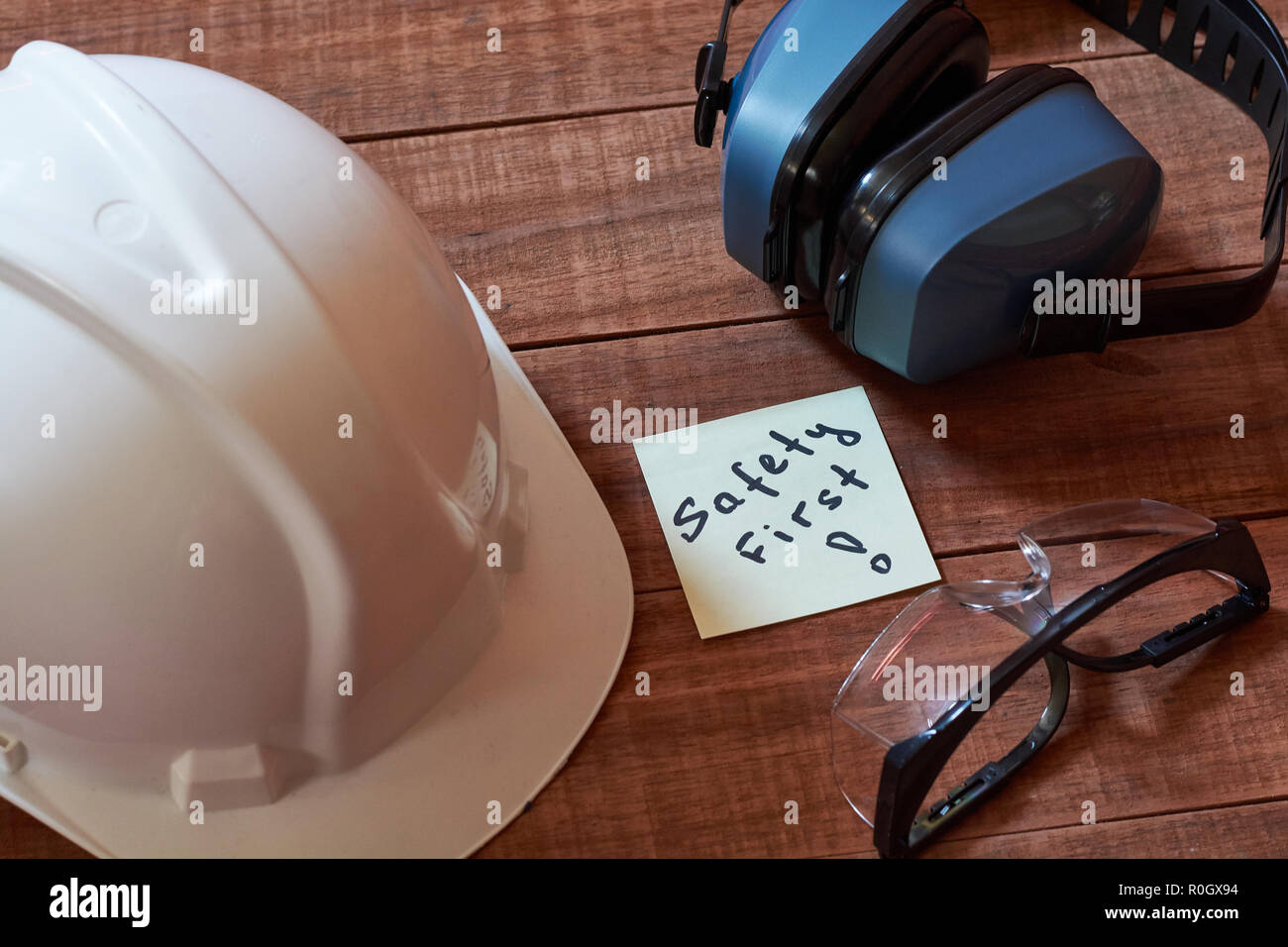 Safety first Hinweis einer gelben Stück Papier, auf Holz- Hintergrund mit vollständigen persönlichen Schutzausrüstung: Helm, safet Gläser und Ohr p Stockfoto