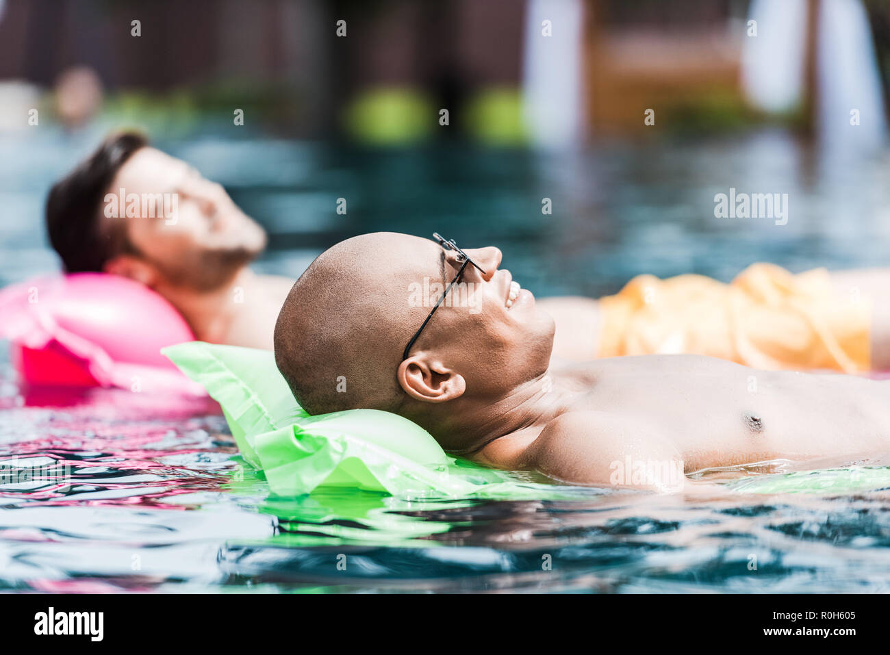 Gerne männliche Freunde Ausruhen und Sonnenbaden auf Luftmatratzen im Pool Stockfoto