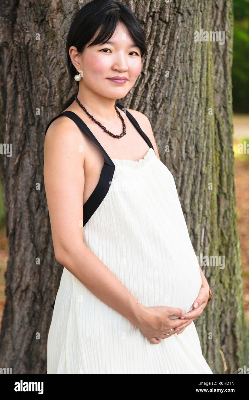 Junge schwangere Frau lächelnd in der Nähe von Tree in Park Stockfoto