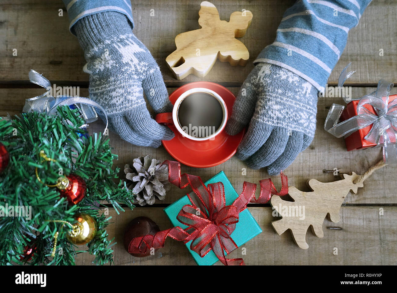 Topview touristische tragen Sie Handschuhe und heißen Kaffee Tasse auf Holz Tisch, die Geschenke Weihnachten Thema dekorieren halten Stockfoto