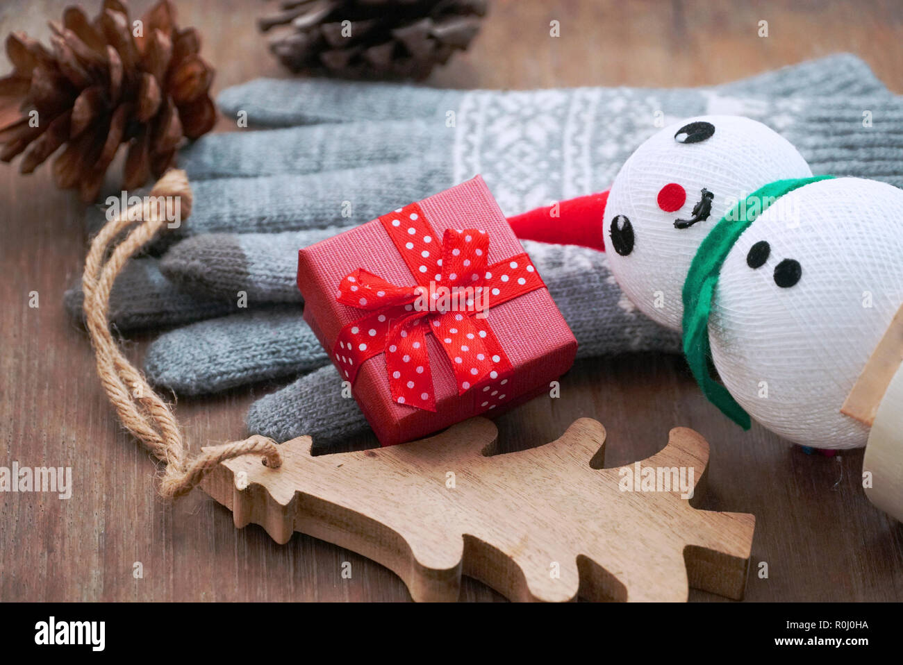 Red Geschenkboxen in der Nähe von Handschuhen und Tannenzapfen und Schneemann und kleinen Holz Weihnachtsbaum auf den Tisch dekorieren Stockfoto