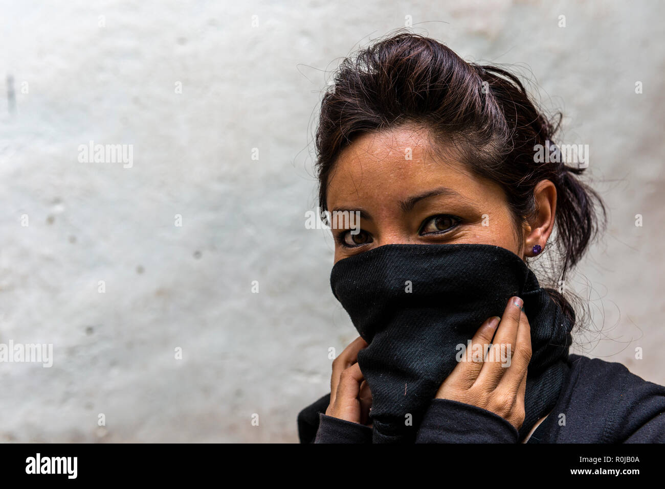 Das Porträt einer jungen lokalen Frau, die ihr Gesicht von der Kälte durch einen schwarzen Schal. Stockfoto