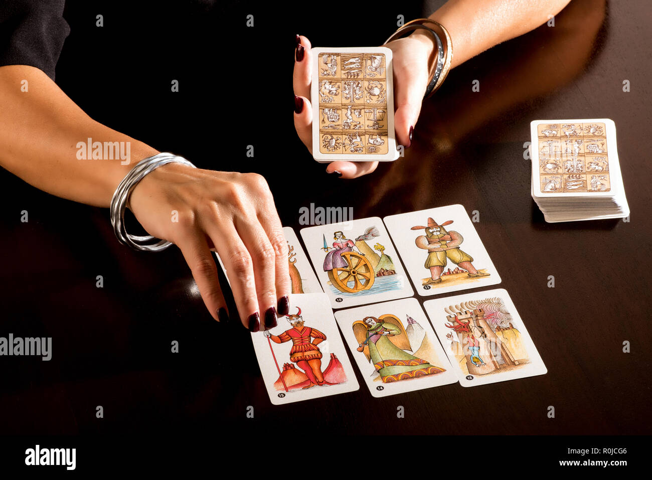 Wahrsagerin liest ein Deck von bildliche symbolische Tarot Karten in Nahaufnahme auf ihre Hände, Sie zur Festlegung auf einen Tisch ihr Weissagen zu machen Stockfoto