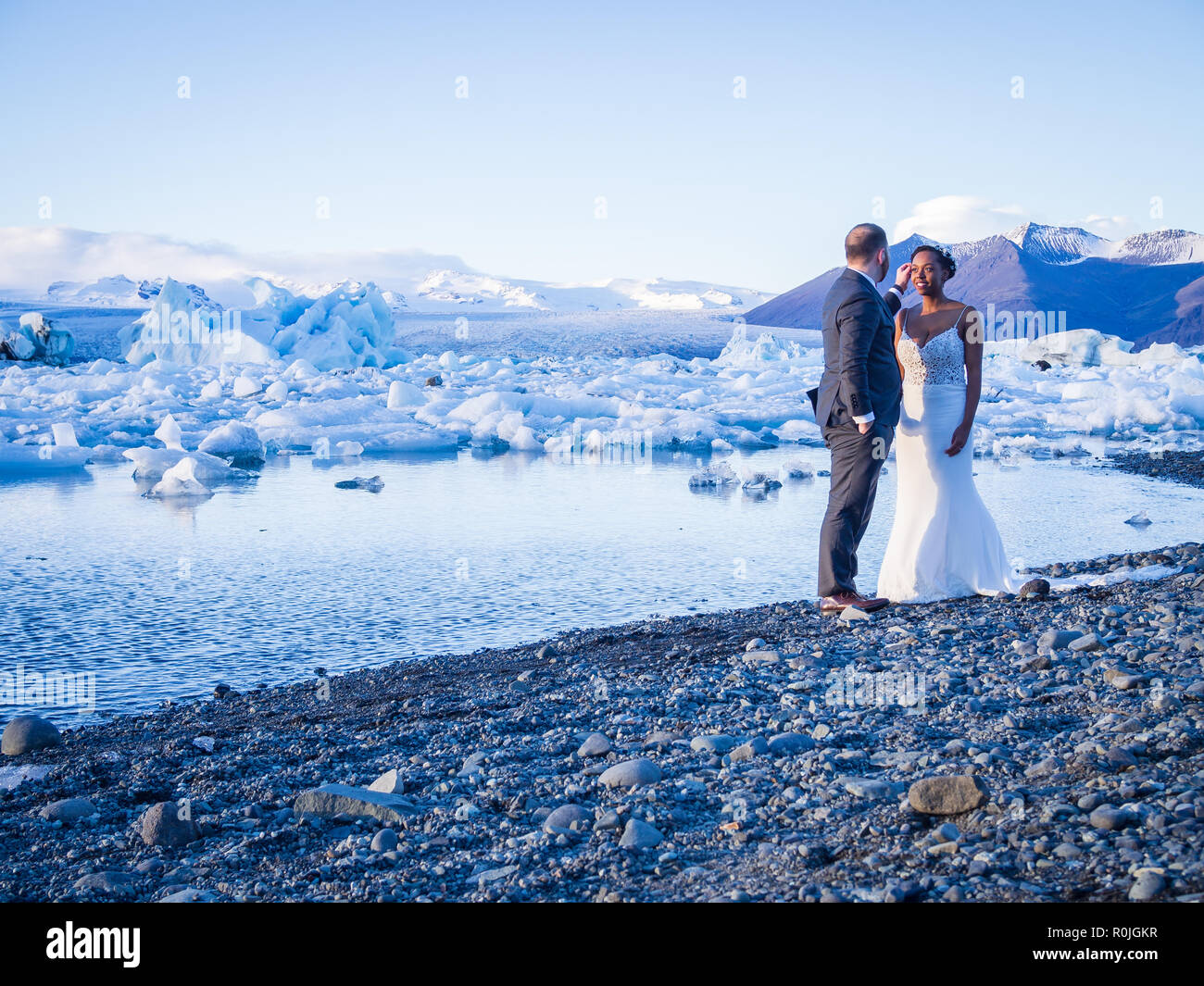 JOKULSARLON, ISLAND - 17. OKTOBER 2018: afrikanische Braut und Bräutigam am Gletschersee Jökulsárlón glasier Lagune in Island in Abend Stockfoto