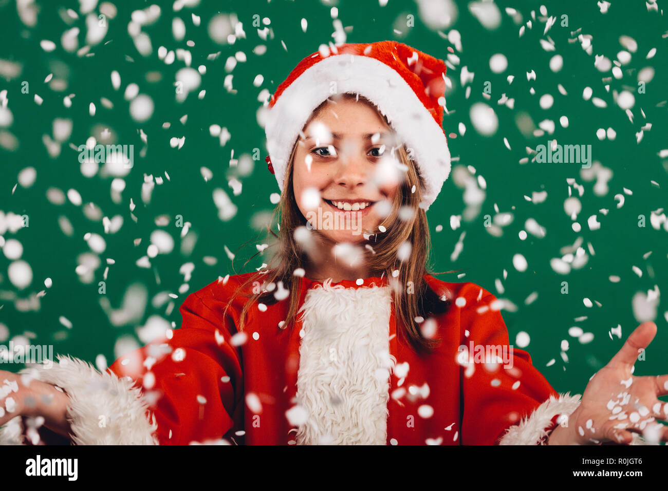 Lächelnde Mädchen in santa claus Kleid vor grünem Hintergrund mit künstlichem Schnee Flocken fallen alle um. Porträt eines lächelnden Mädchen mit Op Stockfoto