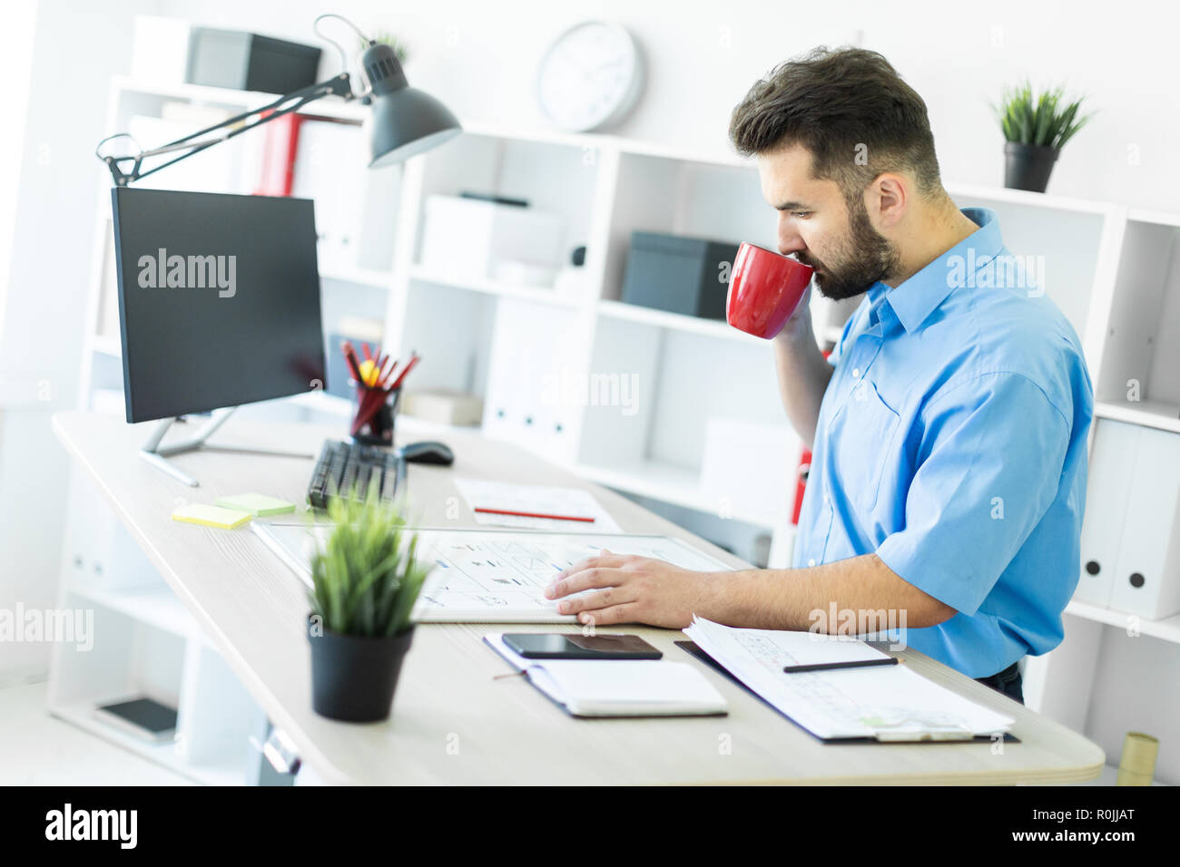 Der junge Mann ist im Büro am Computer Tisch, Kaffee trinken und Arbeiten mit einem