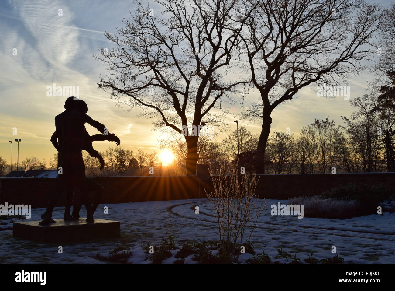 Timeline der aufgehenden Sonne im Winter Sonnenuntergang Himmel aus gesehen hinter dem Bronze Skulptur auf dem Soldatenfriedhof reimsbach an der Saar, Deutschland. Stockfoto