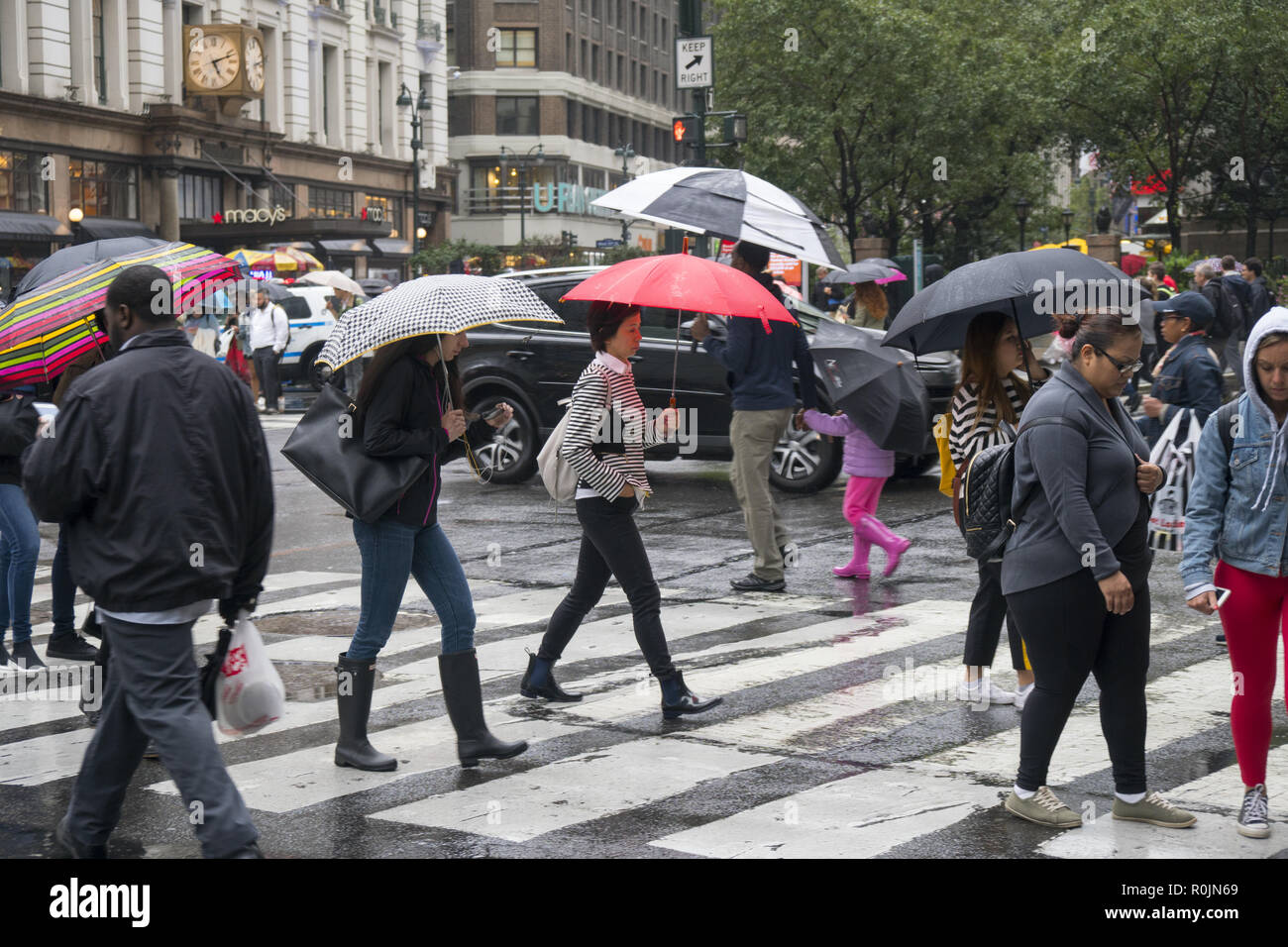 Fußgänger mit Sonnenschirmen, an einem regnerischen Tag in der Nähe von Macy's Kaufhaus an der 34th St. & Broadway in New York City. Stockfoto