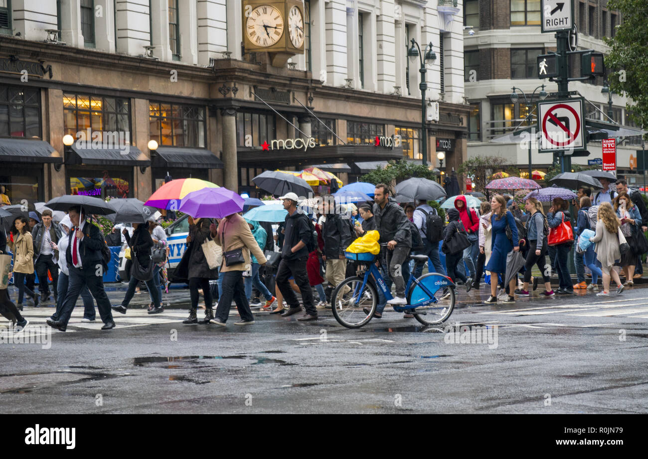 Fußgänger mit Sonnenschirmen, an einem regnerischen Tag in der Nähe von Macy's Kaufhaus an der 34th St. & Broadway in New York City. Stockfoto