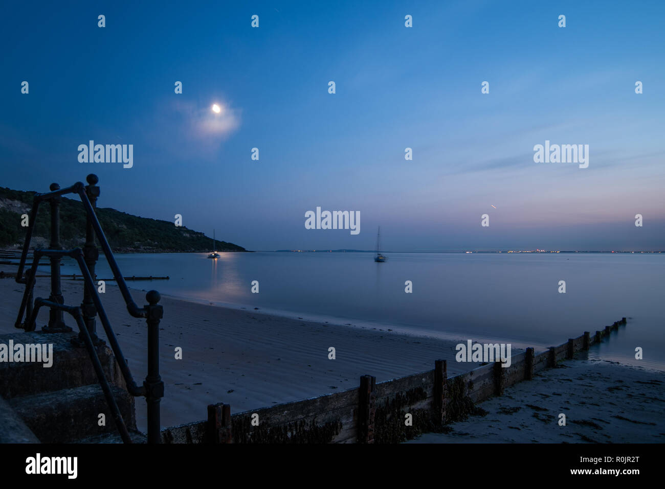 Nachthimmel mit Mond über Totland Bay scheint, werfen ein Schimmer im Meer mit Strand und eine groyne im Vordergrund, in der Isle of Wight Stockfoto