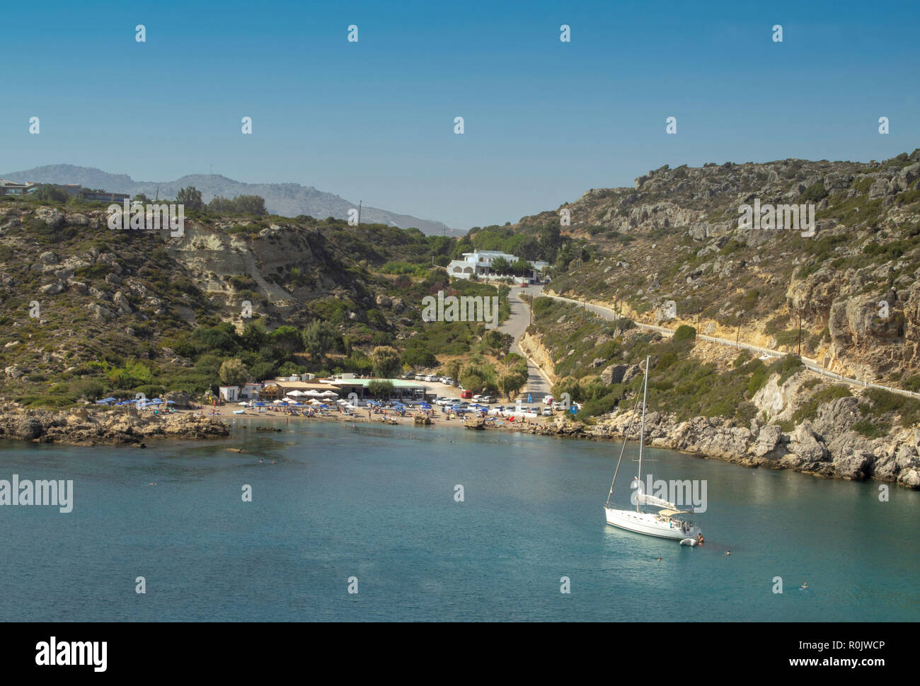 Das klare, blaue Wasser der Anthony Quinn Bucht in Rhodos, Griechenland mit Menschen beim Sonnenbaden am Strand und Schwimmen in der Bucht. Stockfoto