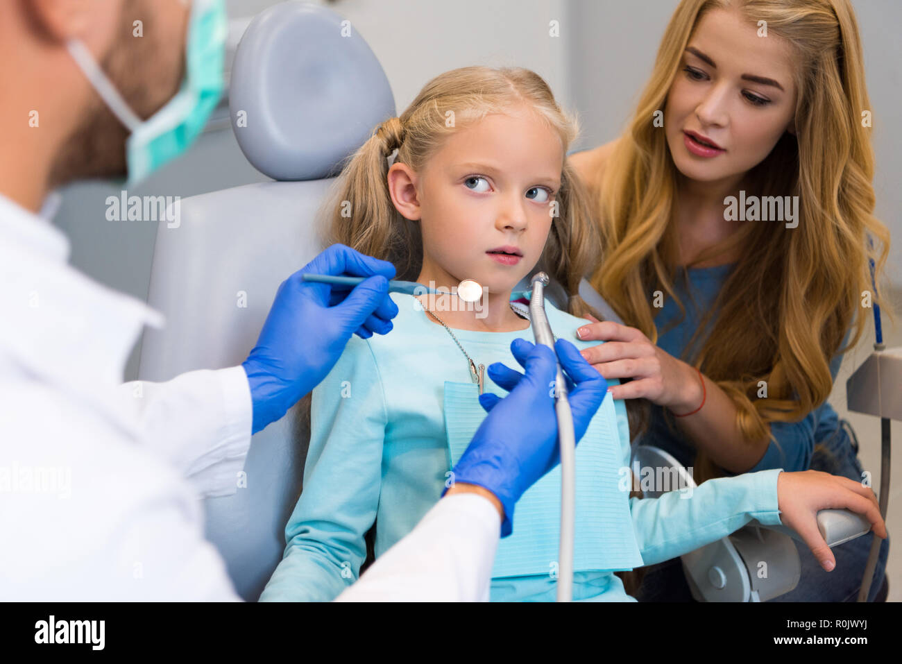 7/8 Schuß von Zahnarzt arbeiten mit verängstigten Kind während Mutter in der Nähe ihrer Sitzung für die Unterstützung Stockfoto