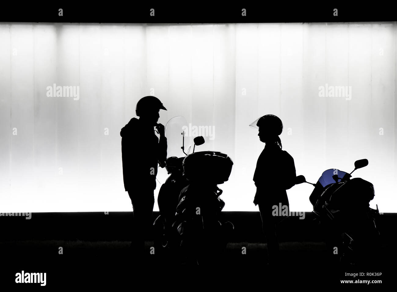 Unscharfe Silhouette des Mannes und der Frau, Helm und Vorbereitung auf einem Motorrad vor modernen Gebäude in der Nacht in Schwarz und Weiß zu sitzen Stockfoto