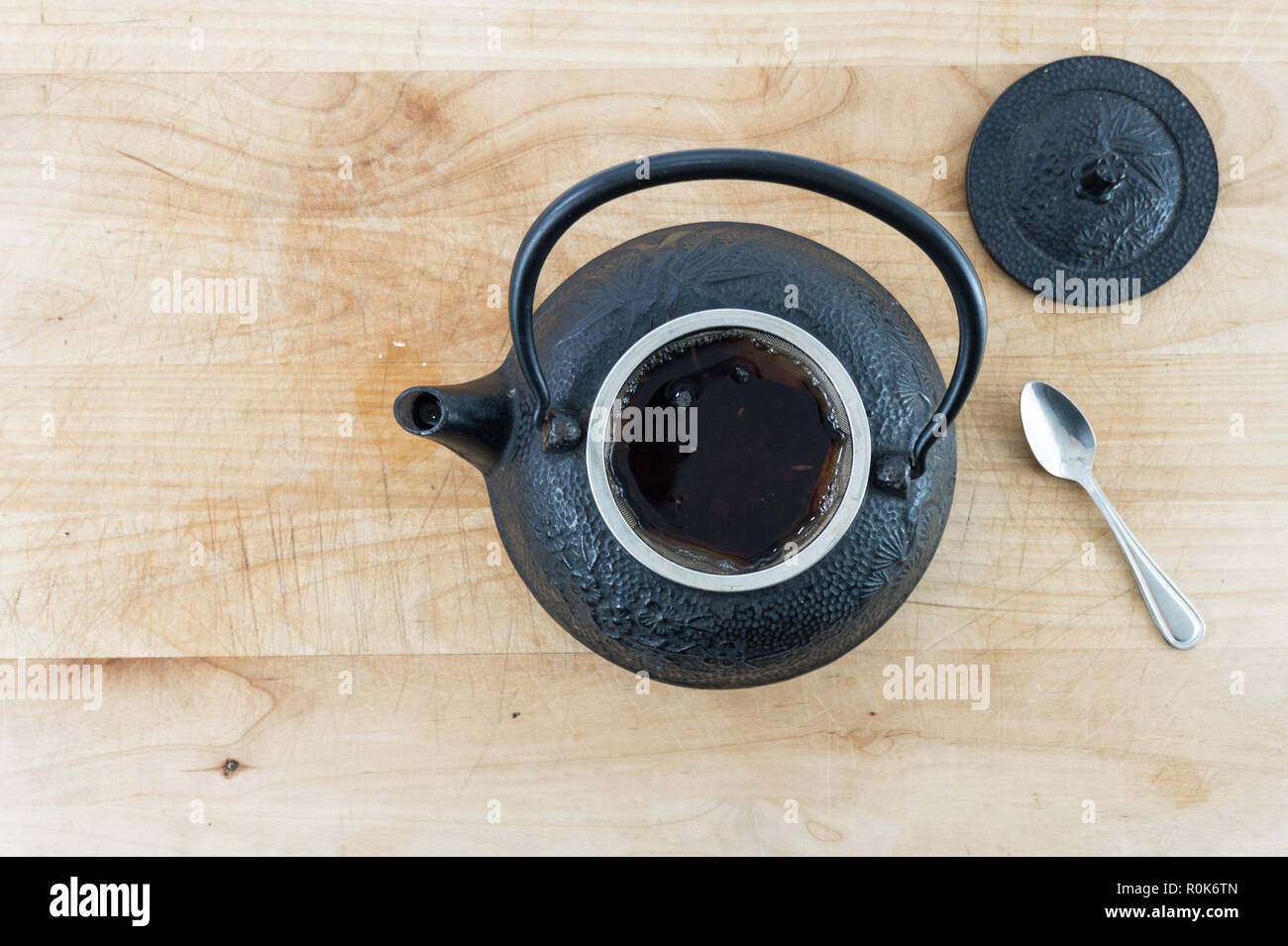 Ansicht von oben schwarz Gusseisen Teekanne voller heißer Tee mit einem Löffel auf eine verblasste Holztisch oder des Fachs Instagram suchen. Hygge. Gemütlich. Stockfoto