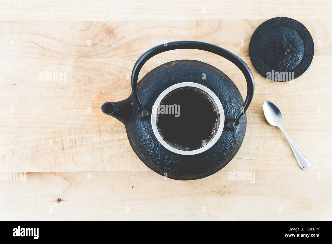 Ansicht von oben schwarz Gusseisen Teekanne voller heißer Tee mit einem Löffel auf eine verblasste Holztisch oder des Fachs Instagram suchen. Hygge. Gemütlich. Stockfoto
