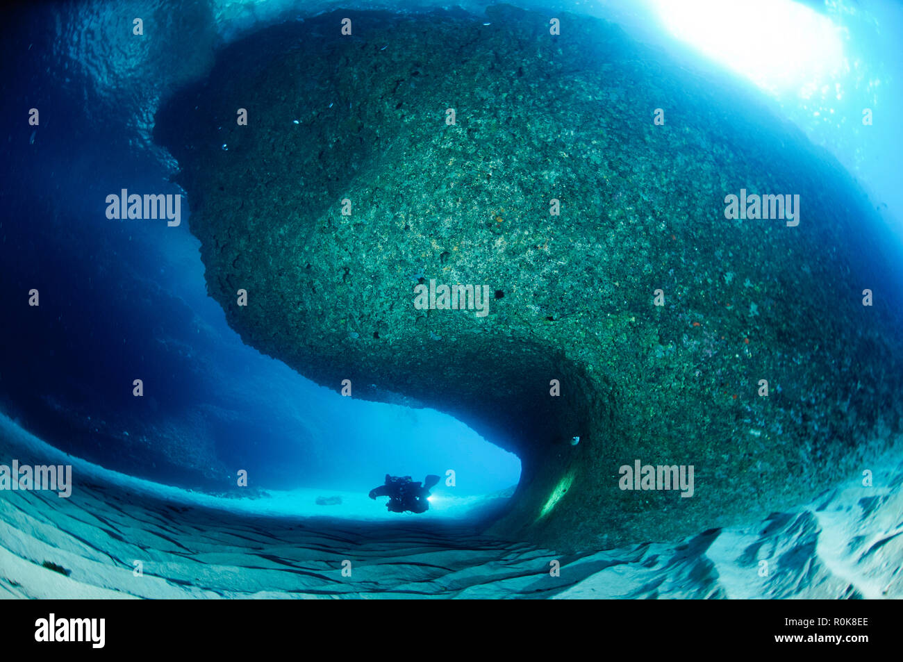Taucher schwimmen um eine große Felsformation in einem offenen Kaverne auf die Kosten von Sardinien. Stockfoto