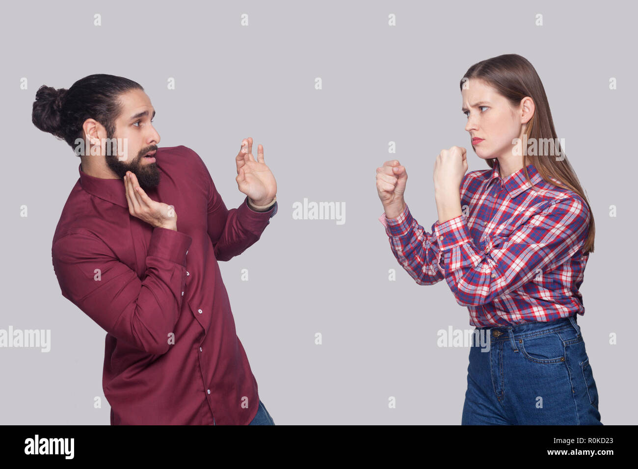 Profil Seitenansicht Portrait von wütenden Frau, die mit dem Boxen Fäuste und bereit, zu verwirrt verängstigt Mann mit schwarzen gesammelt Haar anzugreifen. indoor Stud Stockfoto
