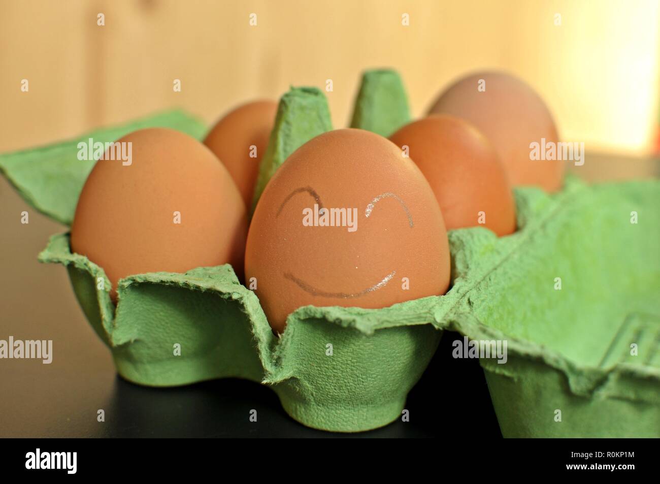 Gruppe von braunen Hühnereier in einem grünen offenen Form - Arbeiten an natürlichen Holz- Hintergrund. Die nächsten Ei ist mit weißen smiley Gesicht gemalt. Nahaufnahme Stockfoto