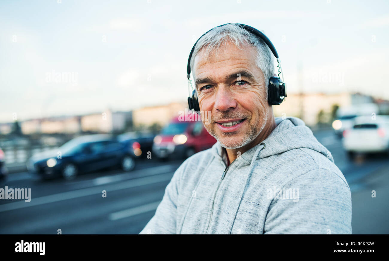 Reife männliche Läufer mit Kopfhörer draußen in der Stadt, Musik hören. Stockfoto