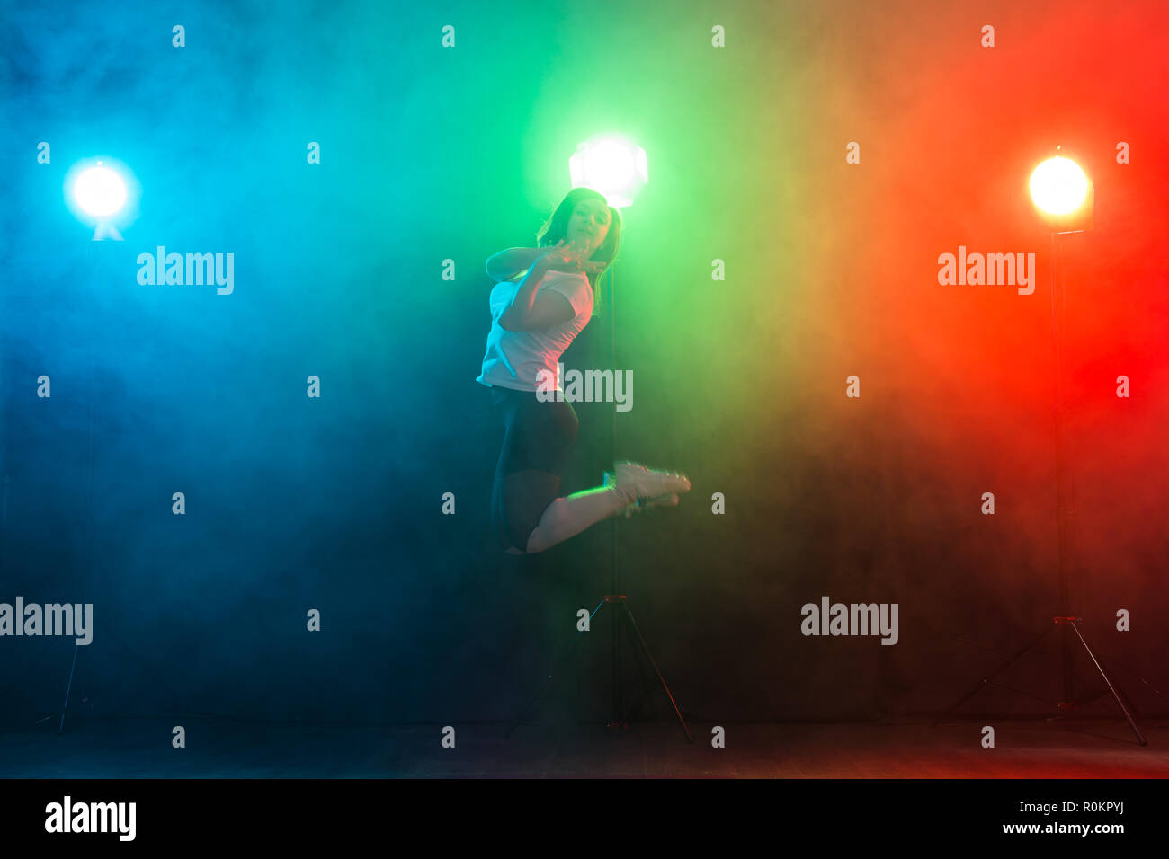 Tanzen, Sport, Jazz Funk und Personen Konzept - junge Frau Sprung in der Dunkelheit unter bunte Licht Stockfoto