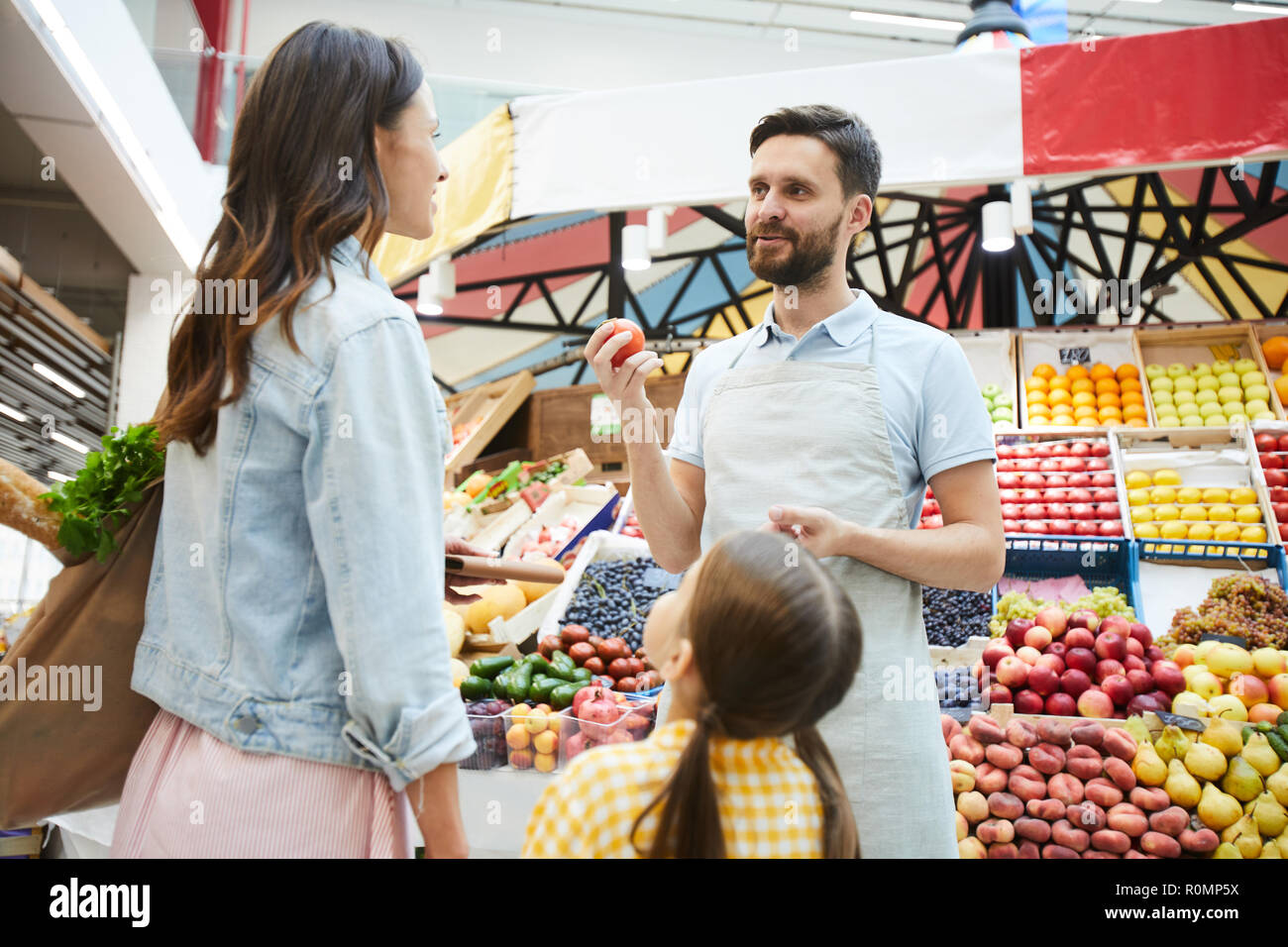 Inhalt hübscher junger Lebensmittelhändler in Schürze im Gespräch mit Kunden und empfehlen Peach zu kaufen, während frisches Essen bei Farmers Market Stockfoto