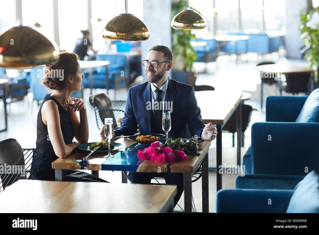 Junge elegantes Paar sitzt von Tisch im Restaurant, im Gespräch und in Champagner und Mittagessen Stockfoto