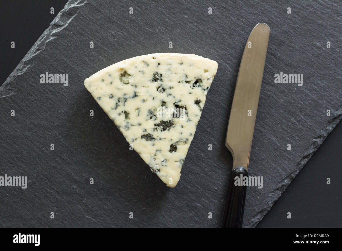 Blue Cheese Dreieck mit Messer auf schwarzem Schiefer Käsebrett isoliert - Roquefort Käse Ansicht von oben Foto Stockfoto