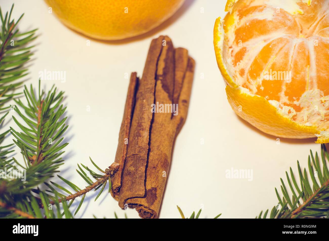 Zwei Mandarinen, von denen einer geschält wird, auf einem weißen Hintergrund. Um die Mandarinen sind Tannenzweigen und ein paar Stöcke von duftenden Zimt. Stockfoto
