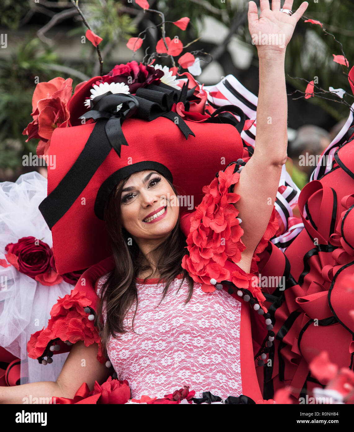 Attraktive junge Dame mit rotem Lippenstift und farbenfrohem Blumenhut während eines Madeira-Blumenfestes. Funchal Madeira Stockfoto