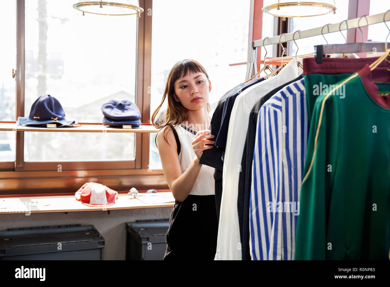 Japanische Verkäuferin in Clothing Store, bei Shirt suchen. Stockfoto
