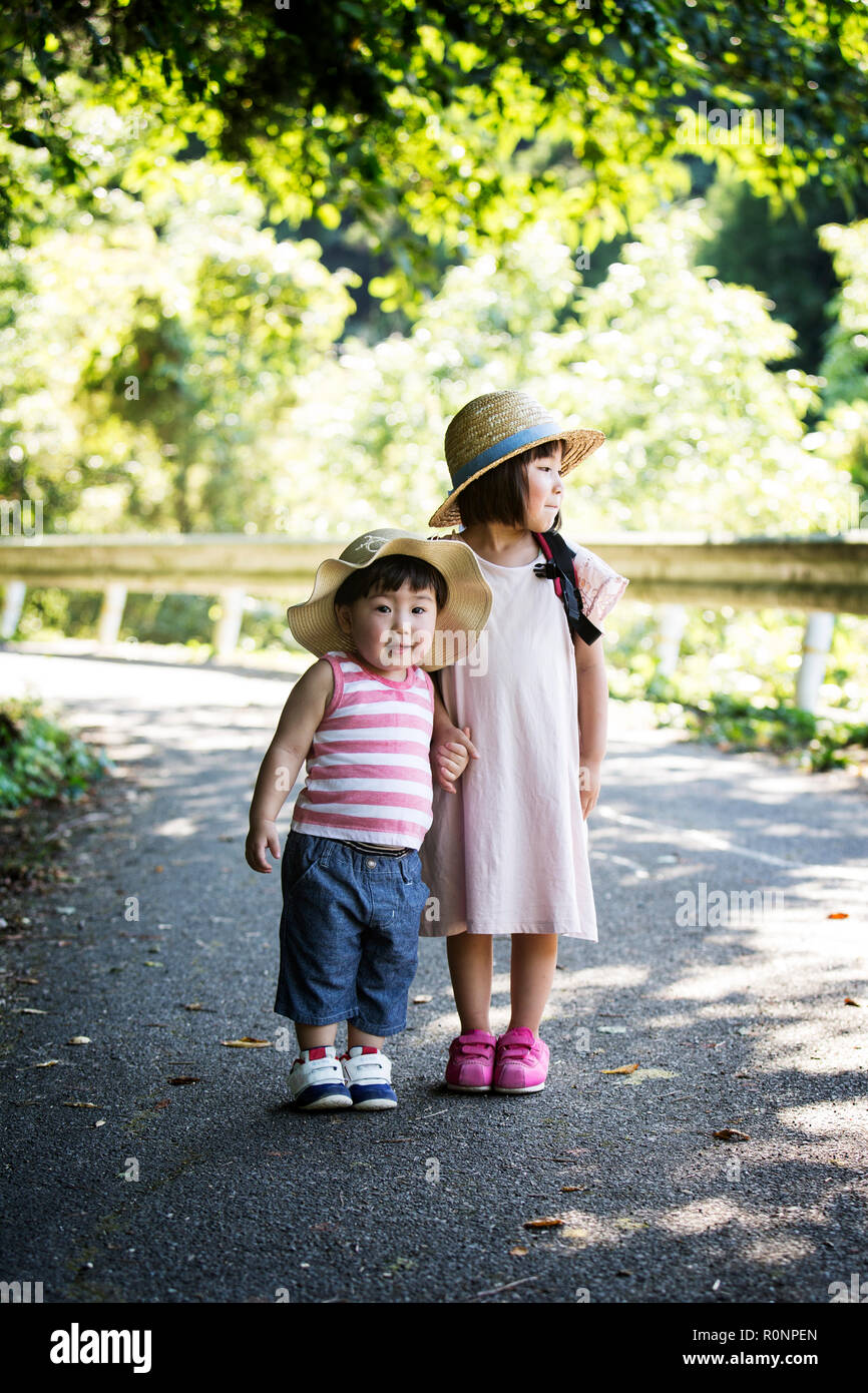 Zwei japanische Mädchen, eine Mütze auf dem Kopf stehend auf Pfad, halten sich an den Händen. Stockfoto