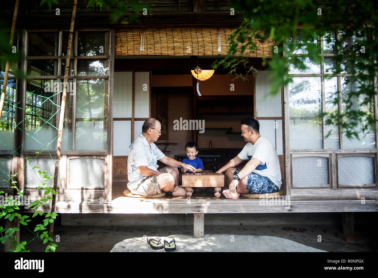 Zwei japanische Männer und wenig Junge sitzt auf dem Boden auf der Veranda der traditionellen japanischen Haus, Spielen gehen. Stockfoto