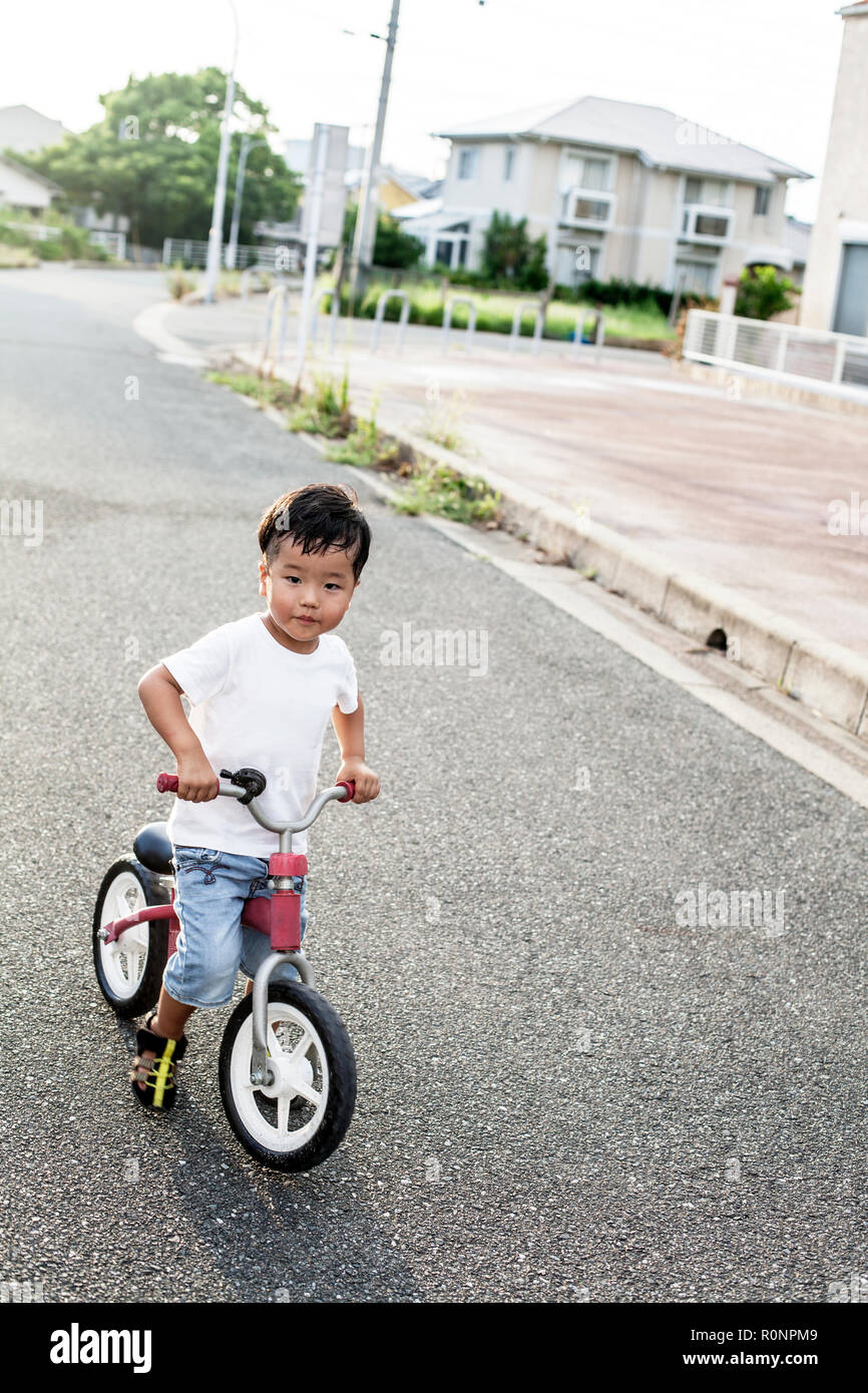 Porträt des japanischen Junge spielt auf der Straße mit einem Fahrrad, auf Kamera schaut. Stockfoto