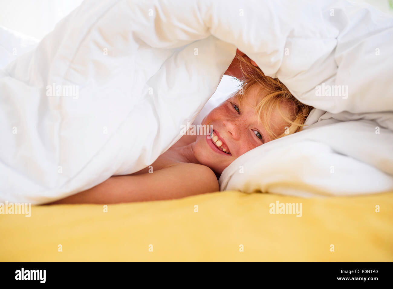 Lächelnde Junge im Bett unter der Bettdecke verstecken Stockfoto