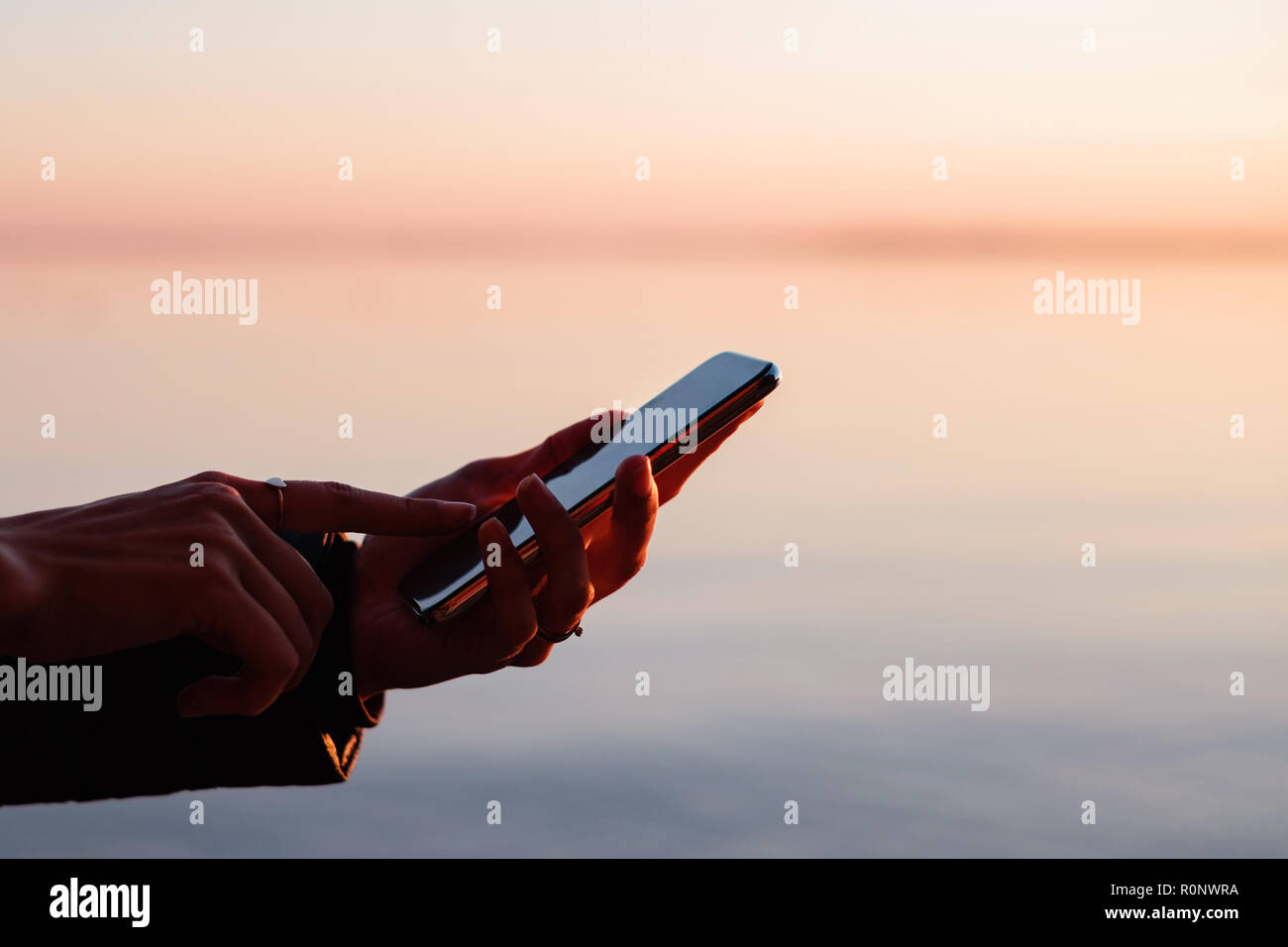 Frau, die draußen über ein Mobiltelefon bei Sonnenuntergang Stockfoto