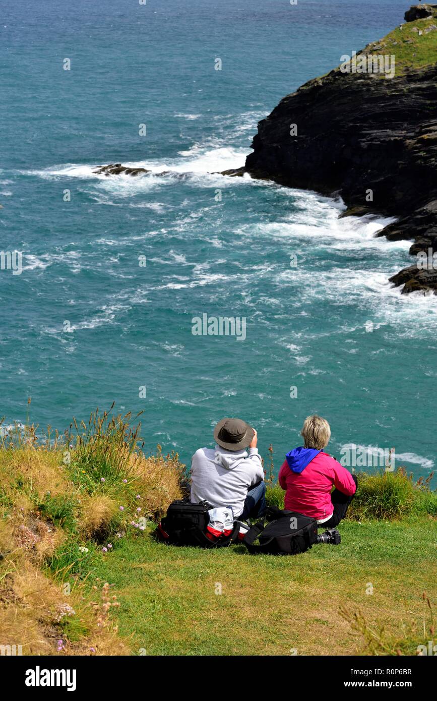 Männliche und weibliche Fotografen ein Foto des kornischen Küste mit Kamera und equiment Taschen hinter ihm, Cornwall, England, Großbritannien Stockfoto