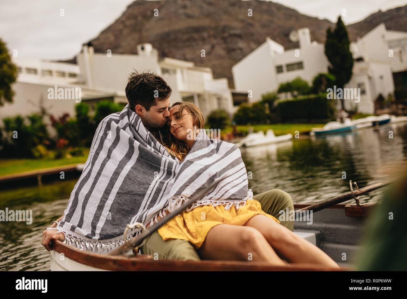 Mann küsste seine Freundin in einem Boot sitzen, während auf einem Datum an einem See. Junges Paar in ein Handtuch eingewickelt in einem Boot sitzen entspannt Zeit bereitgestellt Stockfoto