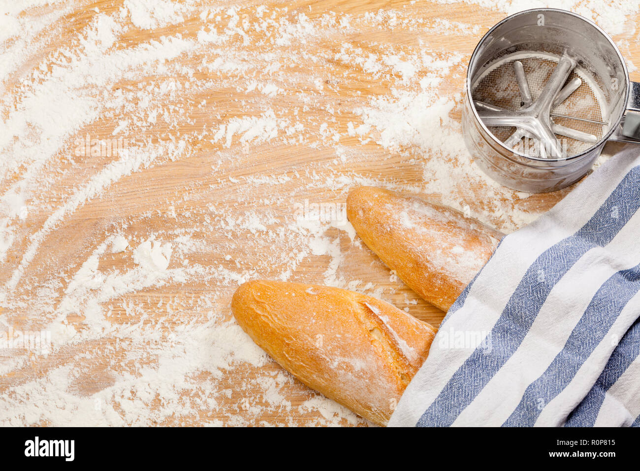 Frisch gebackene handwerklichen Baguettes (französisches Brot) mit Handtuch mit Mehl Sieb oder Sichter auf Holzuntergrund mit Mehl abgedeckt Stockfoto