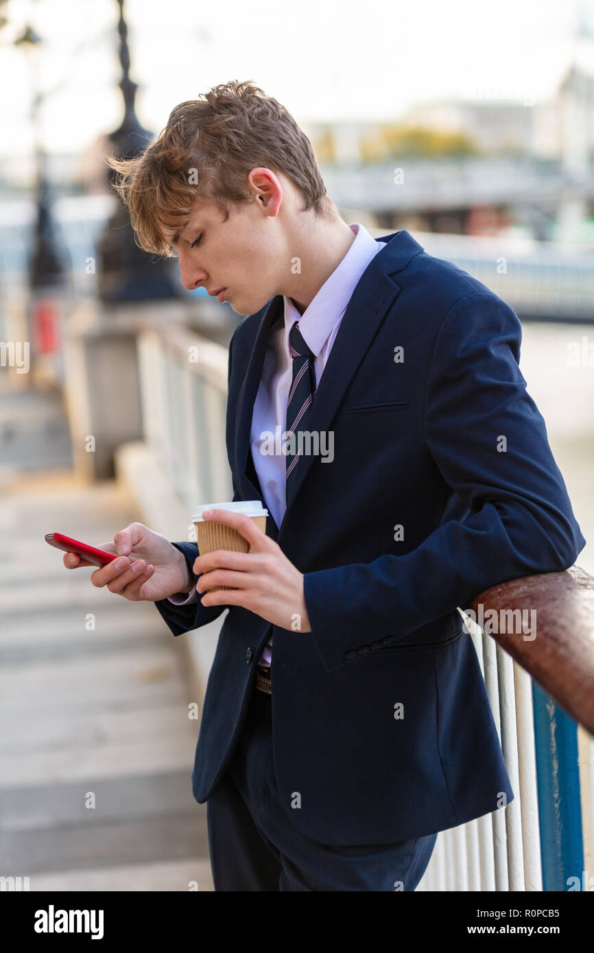 Männliche junge Erwachsene Teenager tragen Anzug und Krawatte mit Smart Handy für Social Media und trinken Kaffee zum Mitnehmen Stockfoto