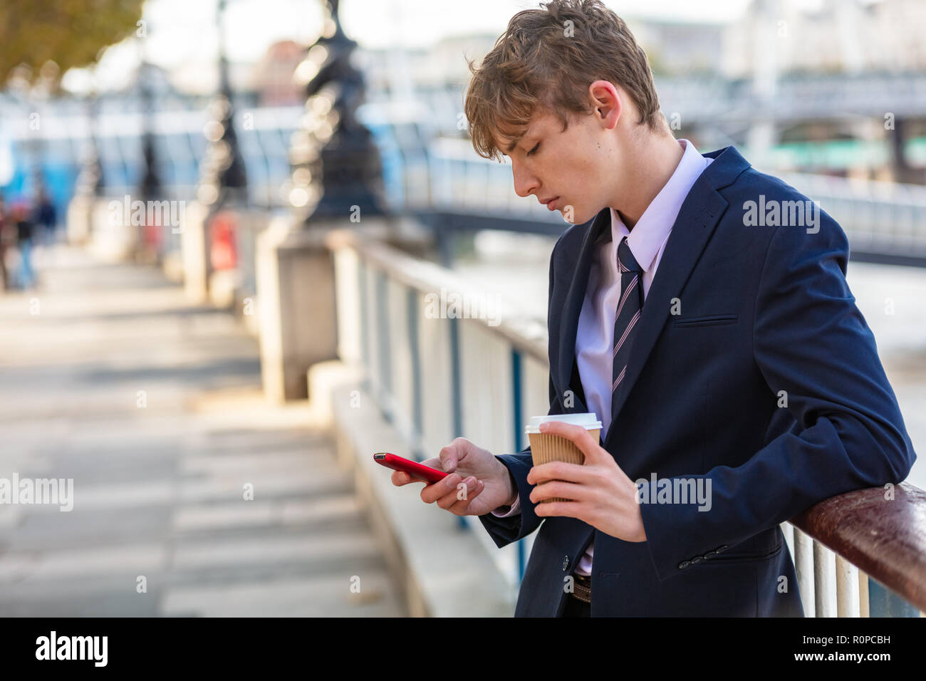 Männliche junge Erwachsene Teenager tragen Anzug und Krawatte mit Smart Handy für socail Medien und trinken Kaffee zum Mitnehmen Stockfoto