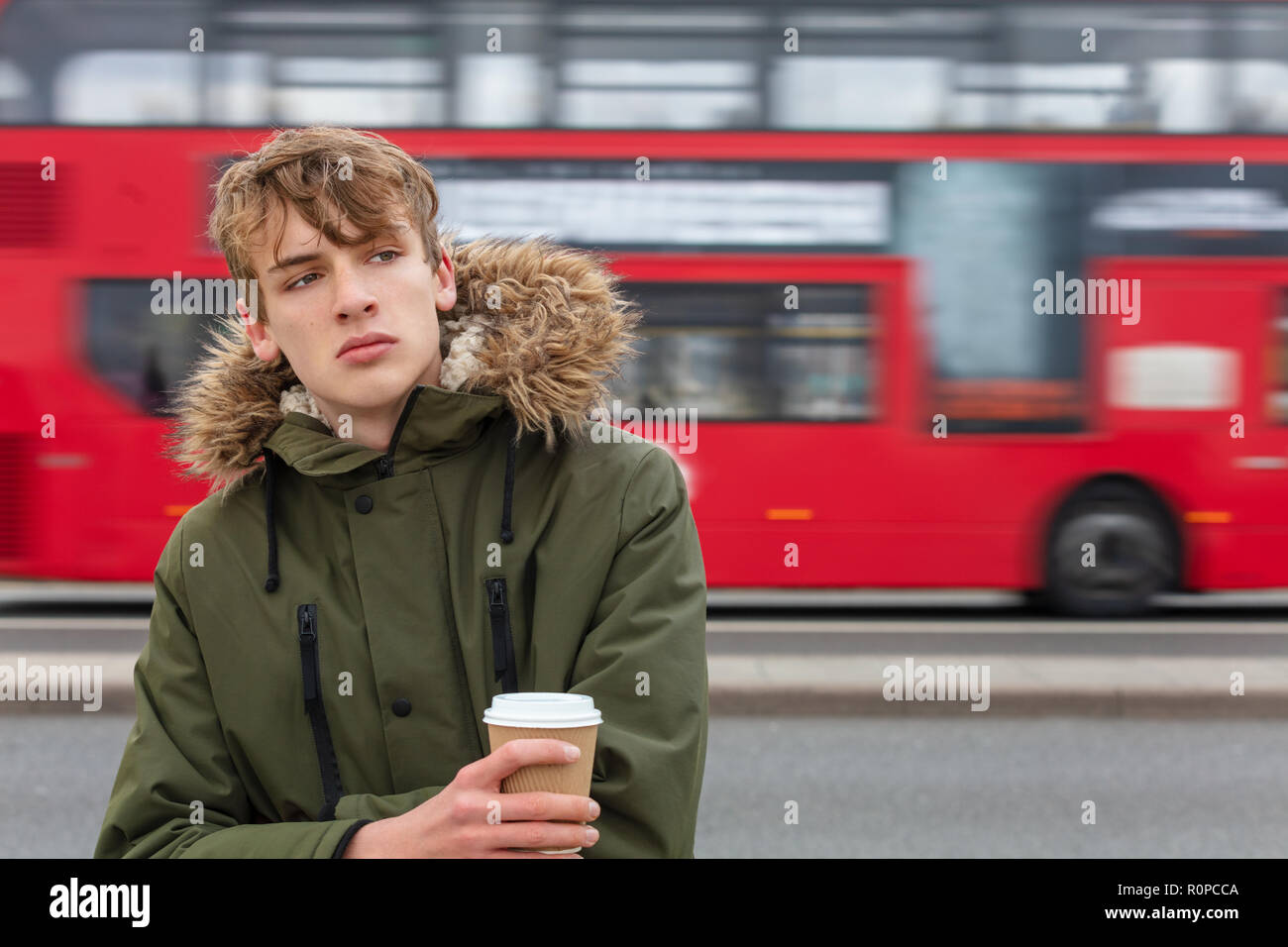 Nachdenkliches traurig, deprimiert, männliche Junge Erwachsene Teenager tragen parka Jacke trinken takeout Kaffee in London stehen auf der Straße vor dem Verschieben Stockfoto