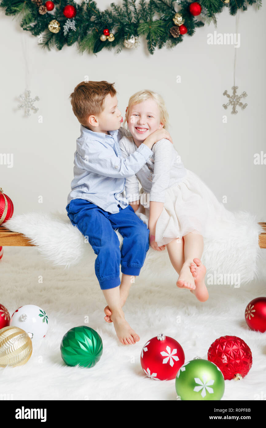 Portrait von weissen Kaukasischen Kinder Freunde sitzen zusammen umarmen Küssen feiern Weihnachten oder Neujahr. Little cute adorable Junge und Mädchen pla Stockfoto