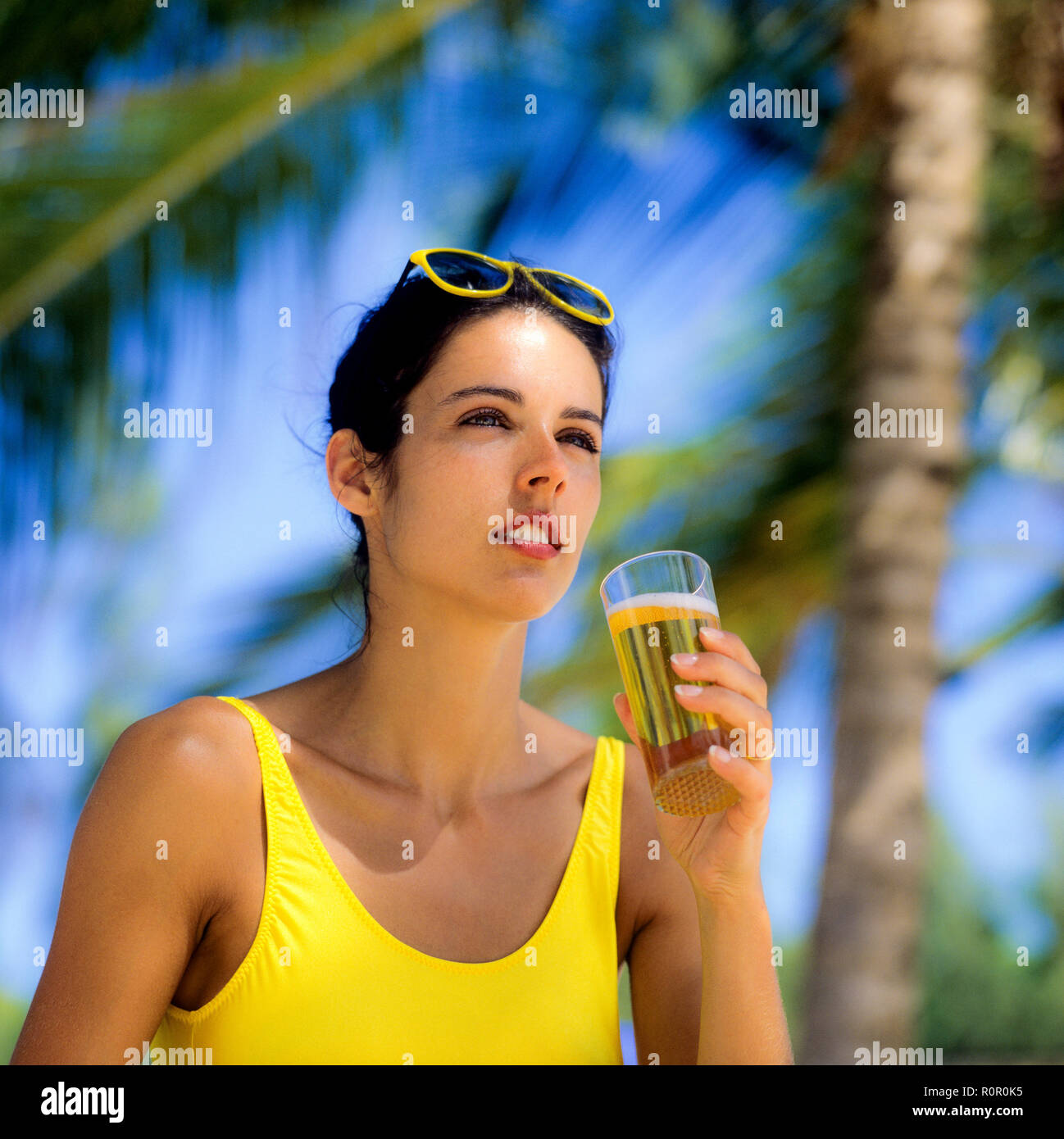 Junge Frau mit gelben Badeanzug mit einem Glas Bier, Palmen Hintergrund, Guadeloupe, Französisch Westindien, Stockfoto