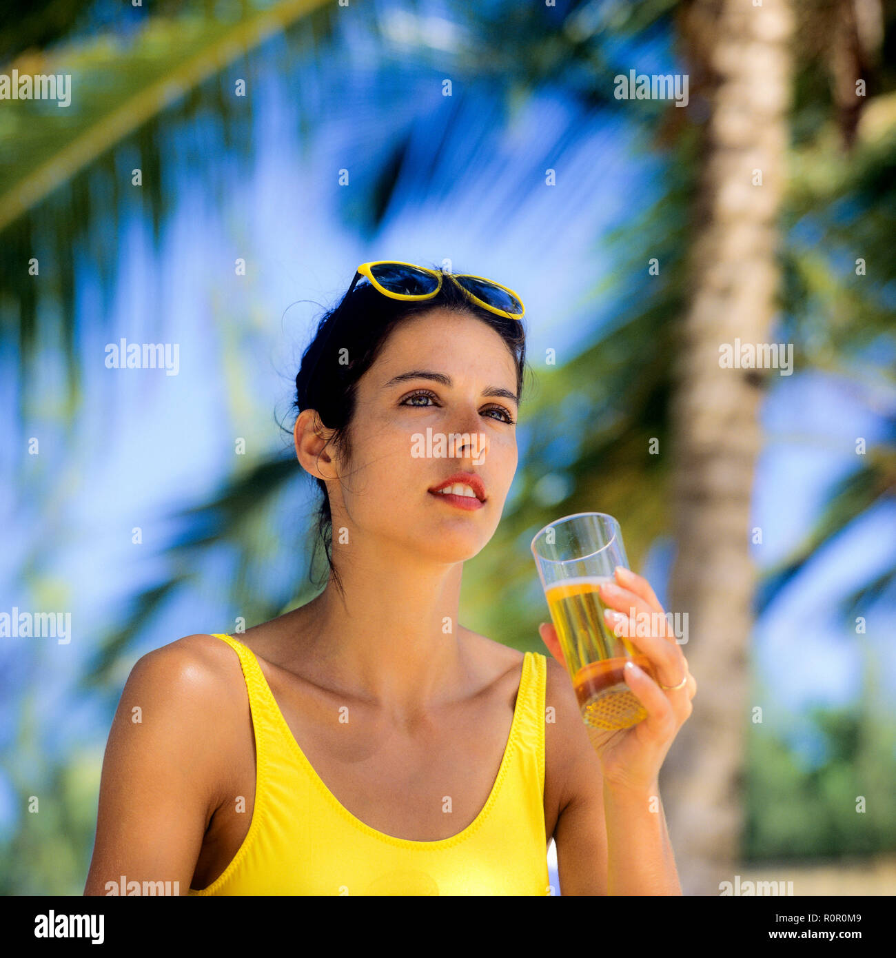 Junge Frau mit gelben Badeanzug mit einem Glas Bier, Palmen Hintergrund, Guadeloupe, Französisch Westindien, Stockfoto