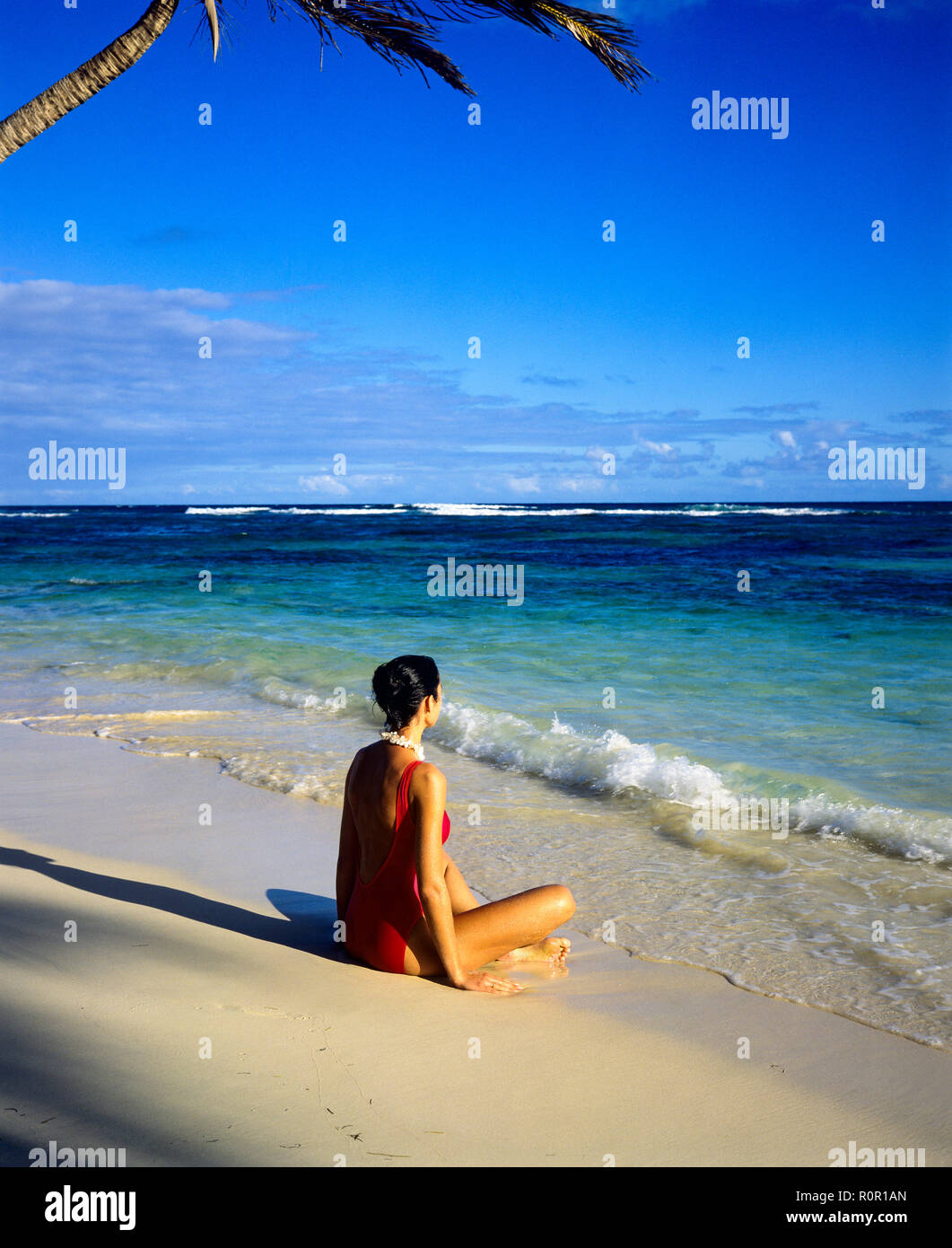 Junge Frau mit roten Badeanzug sitzen auf tropischen Strand und mit Blick auf das Karibische Meer, Guadeloupe, Französisch Westindien, Stockfoto