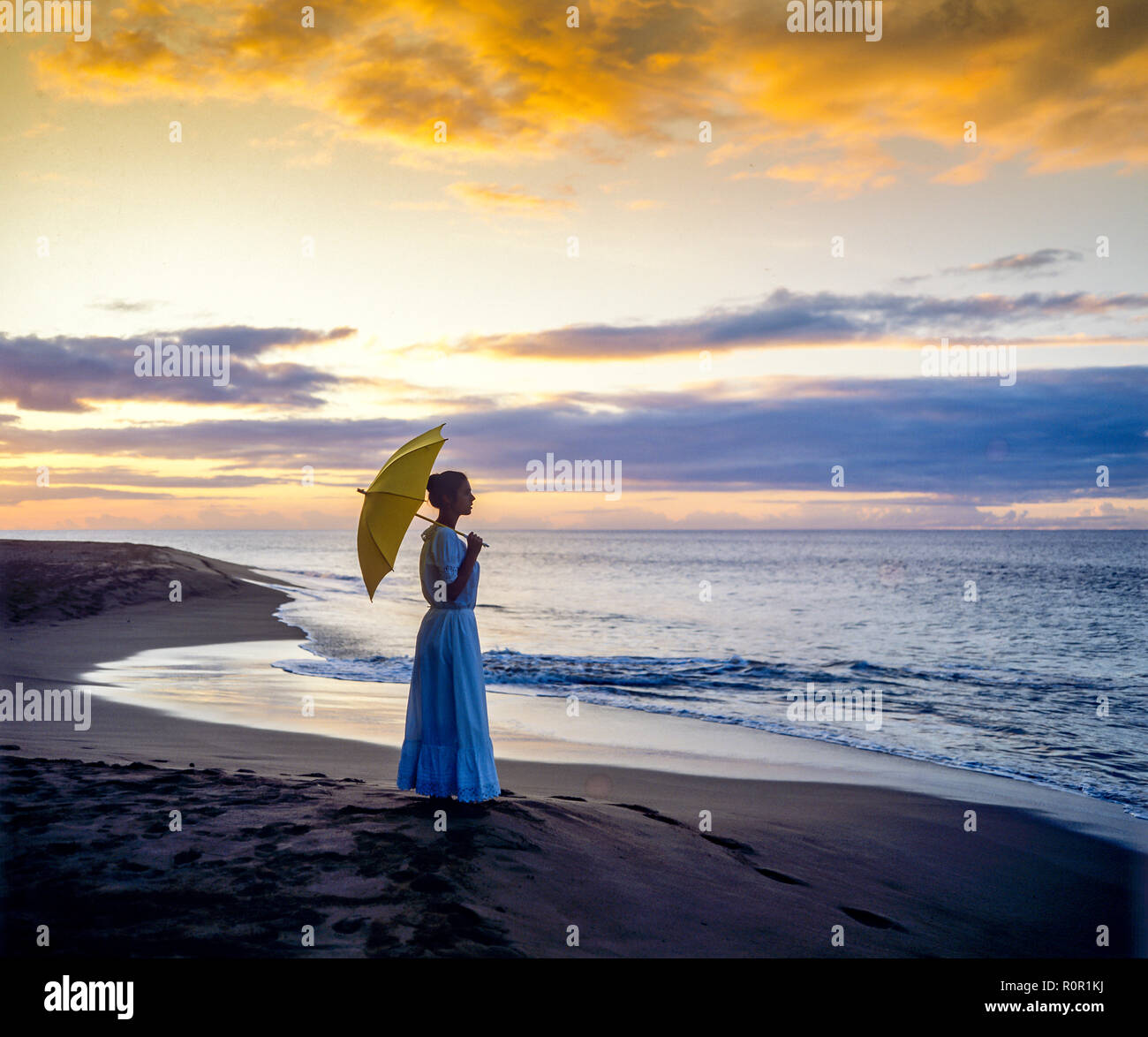 Junge Frau Silhouette mit Kleid und Sonnenschirm mit Blick auf das Karibische Meer bei Sonnenuntergang, tropischen Strand, Guadeloupe, Französisch Westindien, Stockfoto