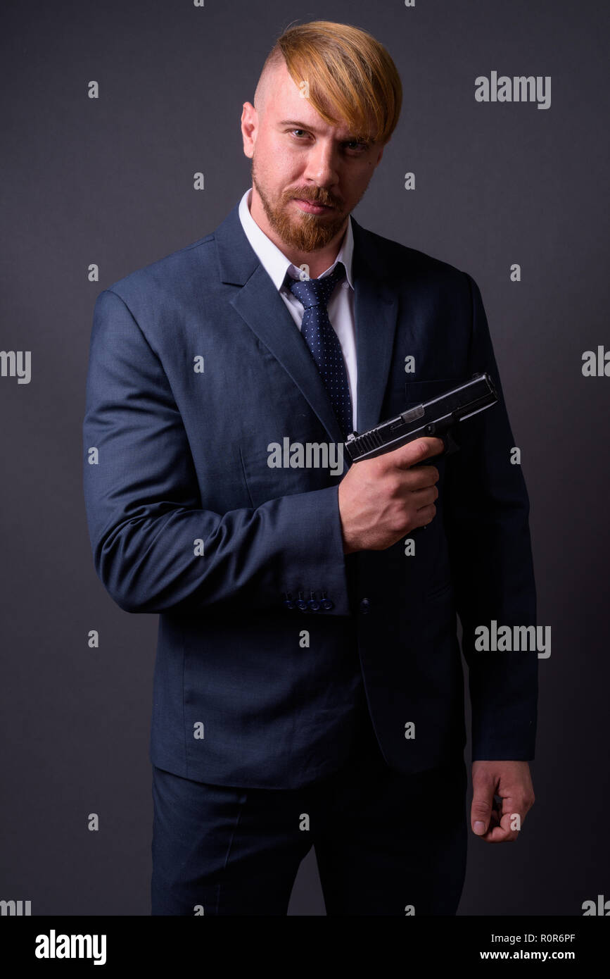 Bärtige Geschäftsmann mit Pistole gegen grauer Hintergrund Stockfoto