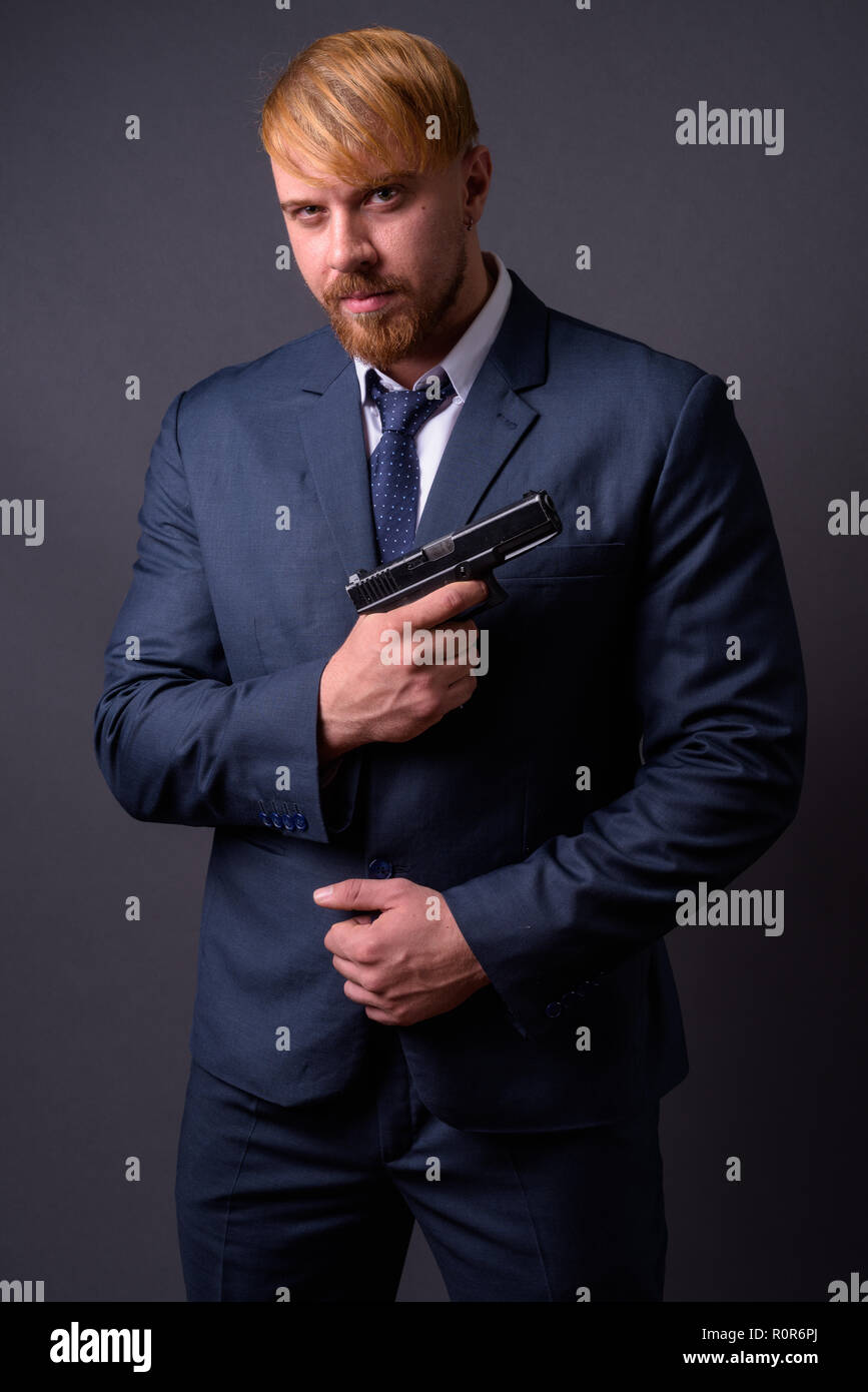 Bärtige Geschäftsmann mit Pistole gegen grauer Hintergrund Stockfoto